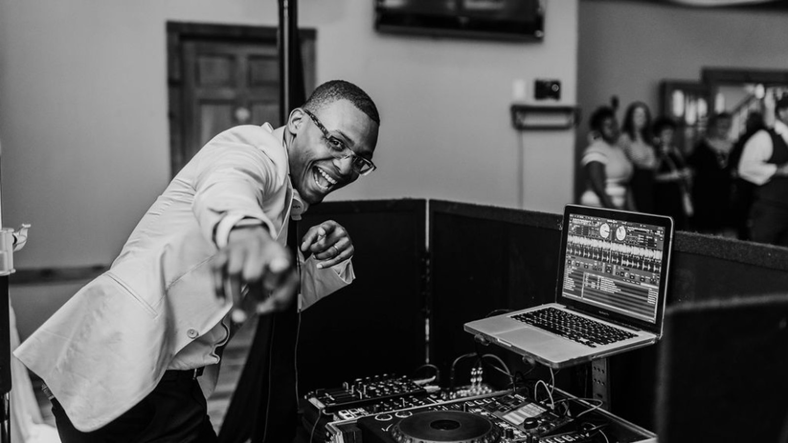 Auburn DJ smiling and pointing from behind the booth at a wedding reception, black and white